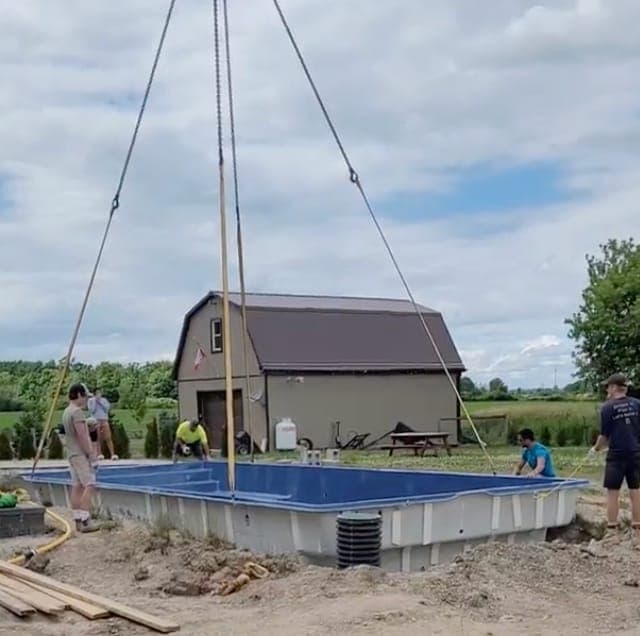 A fibreglass pool shell being craned into a prepared excavation